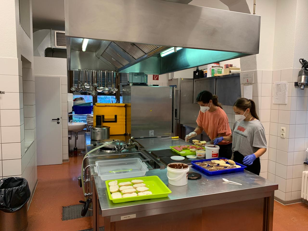 Zwei Frauen mit MAske bei der Zubereitung von Speisen in einer Großküche