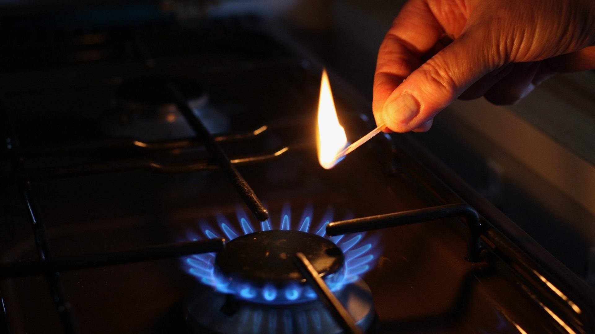 Eine Hand hält ein Streich-Holz über eine Gas-Flamme an einem Herd. Eine Hand hält ein Streich-Holz über eine Gas-Flamme an einem Herd.