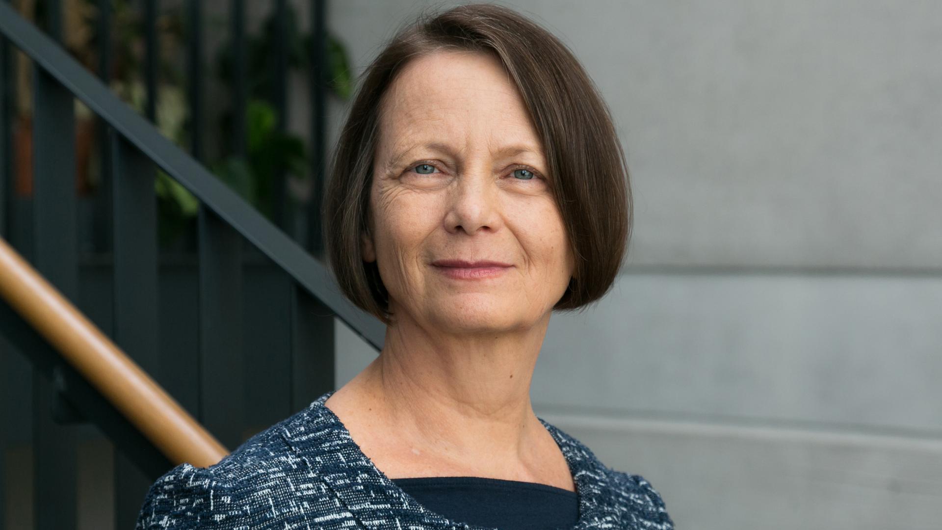 Regina Ammicht Quinn trägt eine blaue Strickjacke und steht im Freien vor einem Treppenaufgang. Regina Ammicht Quinn trägt eine blaue Strickjacke und steht im Freien vor einem Treppenaufgang.