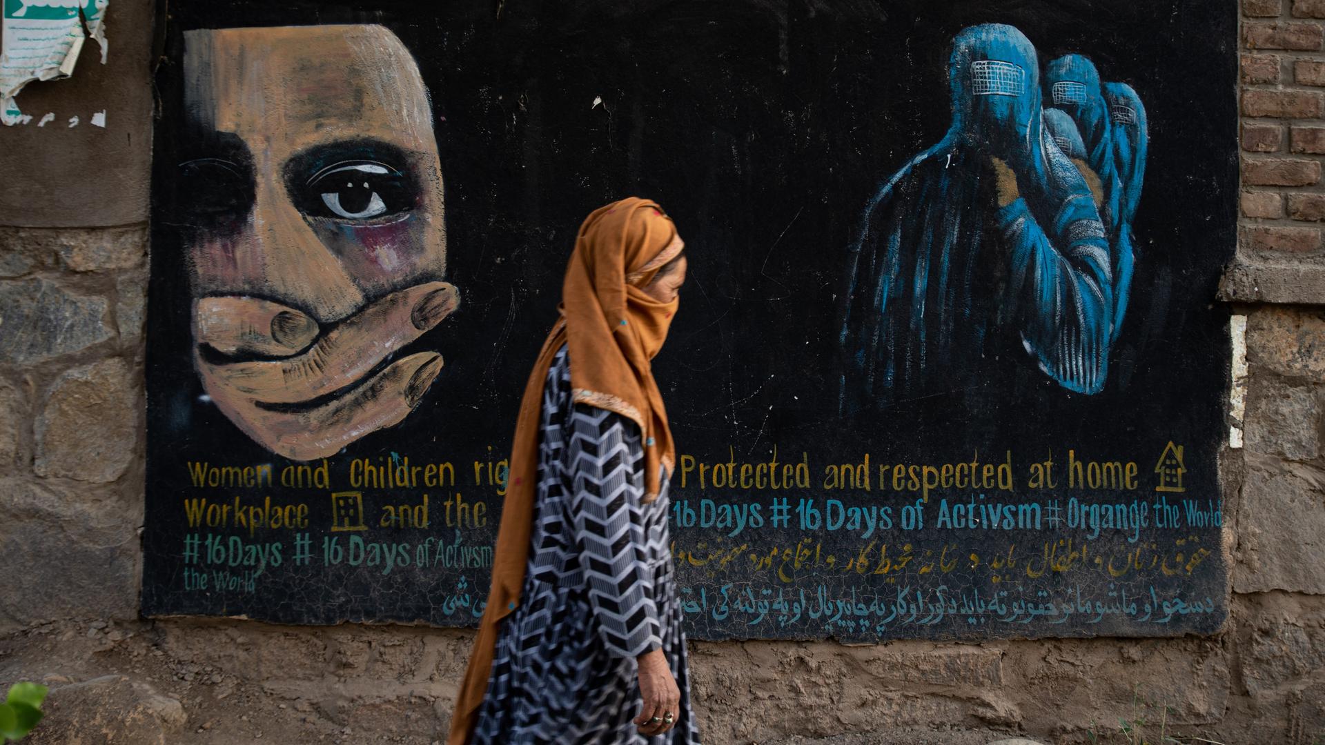Eine verschleierte Frau geht am 12. August 2022 in Bamian, Afghanistan, an einem Wandgemälde vorbei, das die Rechte von Frauen und Kindern in Afghanistan einfordert. 
