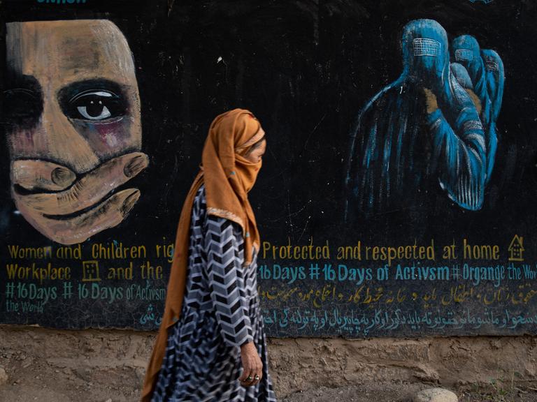 Eine verschleierte Frau geht am 12. August 2022 in Bamian, Afghanistan, an einem Wandgemälde vorbei, das die Rechte von Frauen und Kindern in Afghanistan einfordert. 
