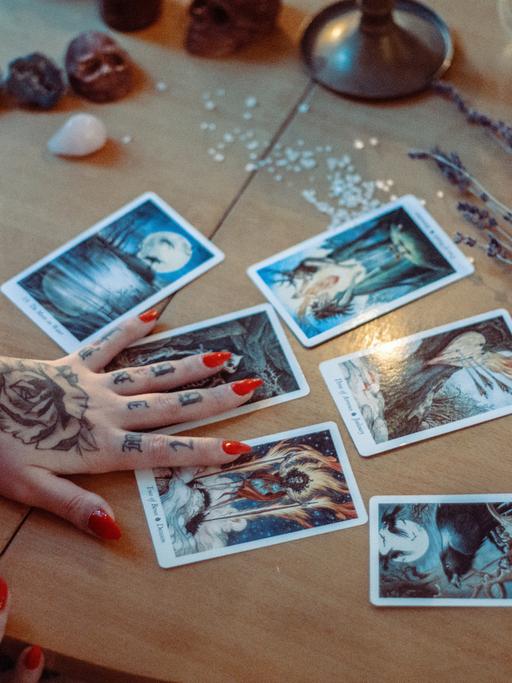 Eine Frau mit Tattoos und roten Fingernägeln legt Tarotkarten