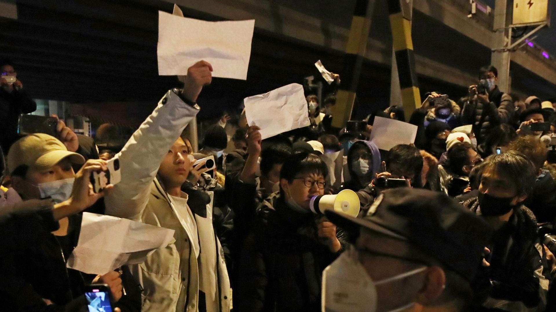 Menschen in Peking stehen teilweise ohne Maske dicht aneinander und halten weißer Blätter hoch. Sie protestieren gegen die strikte Null-Covid-Strategie der Regierung sowie gegen Zensur.