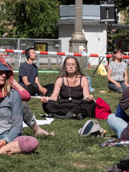 Demonstranten medietieren sitzend auf dem Rasen vor der Volksbühne in Berlin.
