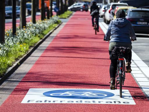 Menschen fahren auf einer roten Fahrradstraße mit ihrem Fahrrad.