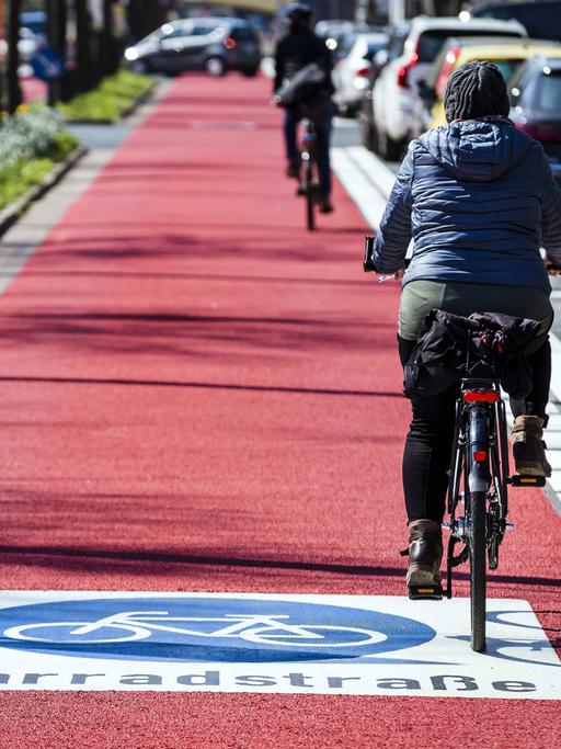 Menschen fahren auf einer roten Fahrradstraße mit ihrem Fahrrad.