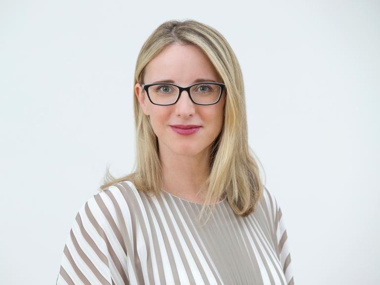 Porträtfoto von Alena Buyx. Die Vorsitzende des Deutschen Ethikrats hat schulterlange blonde Haare, trägt eine schwarze Brille und ein weiß-beige gestreiftes Oberteil. Sie blickt freundlich in die Kamera.