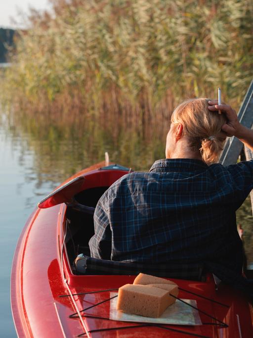 Eine Frau mit Zigarette sitzt in einem Kajak auf einem See.