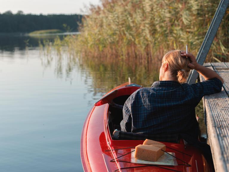 Eine Frau mit Zigarette sitzt in einem Kajak auf einem See.