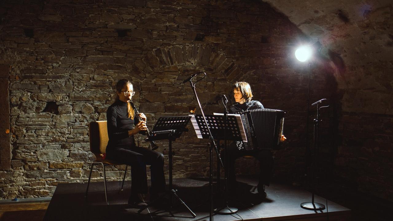 Auf dem Podium eines Konzertkellers sitzen zwei Instrumentalistinnen mit Klarinette und Akkordeon im Scheinwerferlicht Auf dem Podium eines Konzertkellers sitzen zwei Instrumentalistinnen mit Klarinette und Akkordeon im Scheinwerferlicht