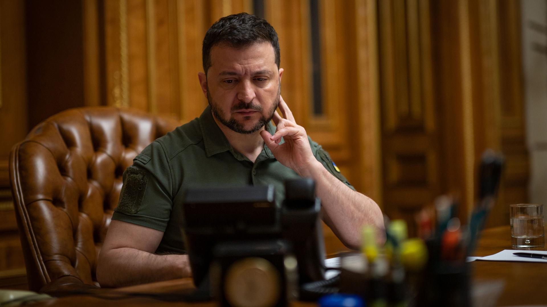 Der ukrainische Präsident Wolodymyr Selenskyj sitzt an einem Schreibtisch und schaut auf ein Telefon. Der ukrainische Präsident Wolodymyr Selenskyj sitzt an einem Schreibtisch und schaut auf ein Telefon.