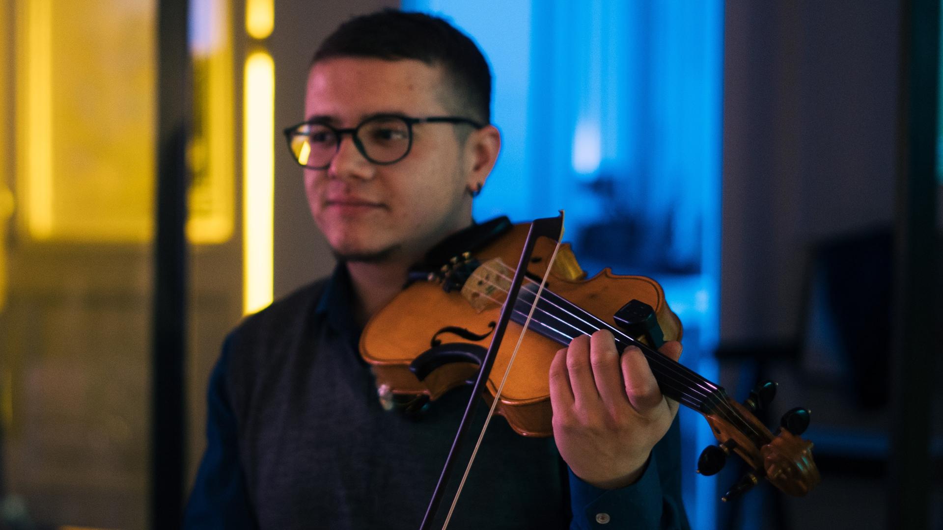 Ein junger Mann spielt Violine, während der Hintergrund des Raumes in den Nationalfarben der Ukraine, gelb und blau, ausgeleuchtete ist. Ein junger Mann spielt Violine, während der Hintergrund des Raumes in den Nationalfarben der Ukraine, gelb und blau, ausgeleuchtete ist.