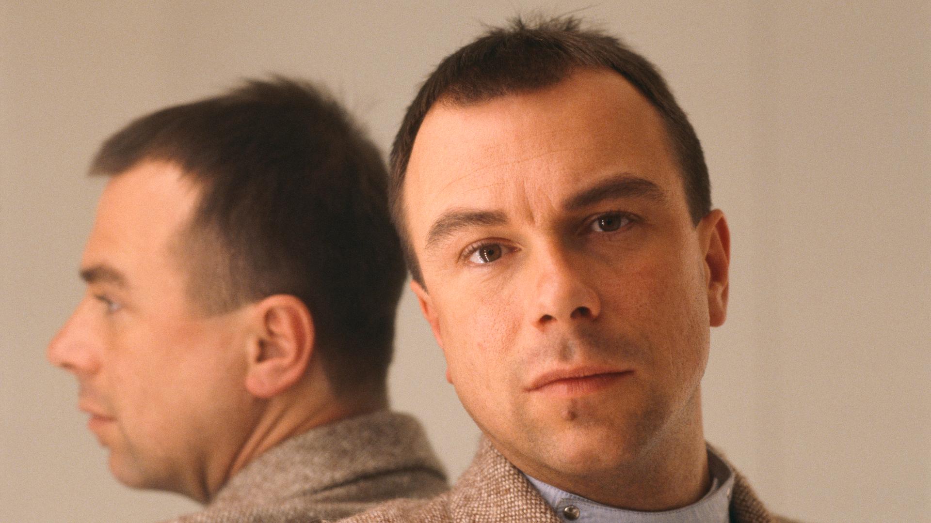 Porträt des Modedesigners Thierry Mugler. Er lehnt an einen Spiegel, wodurch sich sein Kopf spiegelt. Porträt des Modedesigners Thierry Mugler. Er lehnt an einen Spiegel, wodurch sich sein Kopf spiegelt.
