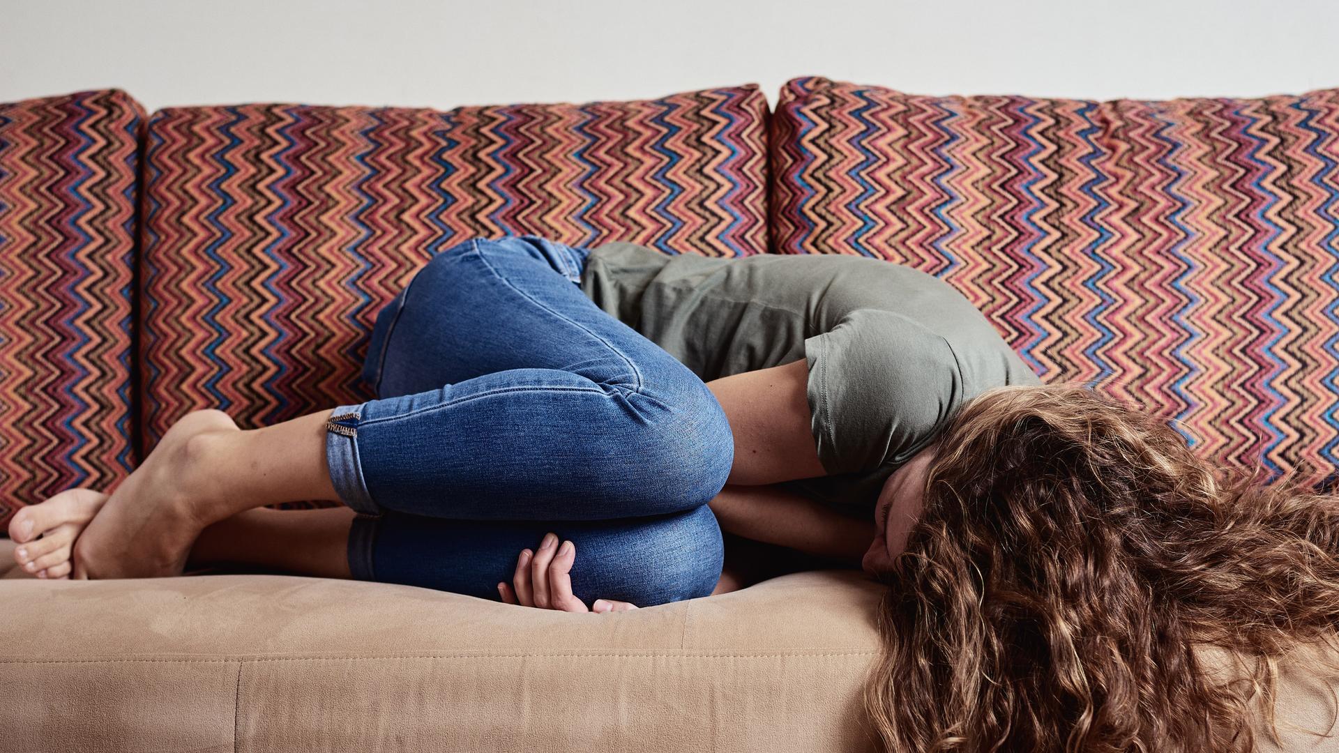 Eine Frau liegt vor Schmerzen zusammengekrümmt auf einem Sofa. Eine Frau liegt vor Schmerzen zusammengekrümmt auf einem Sofa.