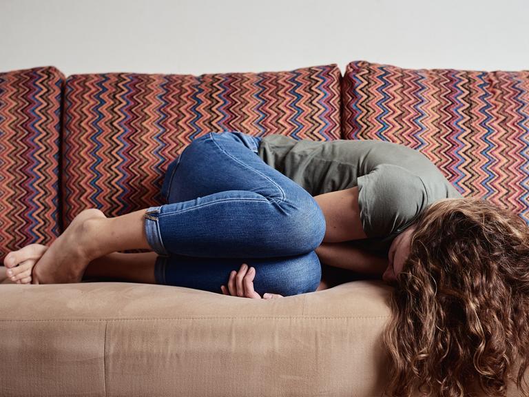 Eine Frau liegt vor Schmerzen zusammengekrümmt auf einem Sofa.