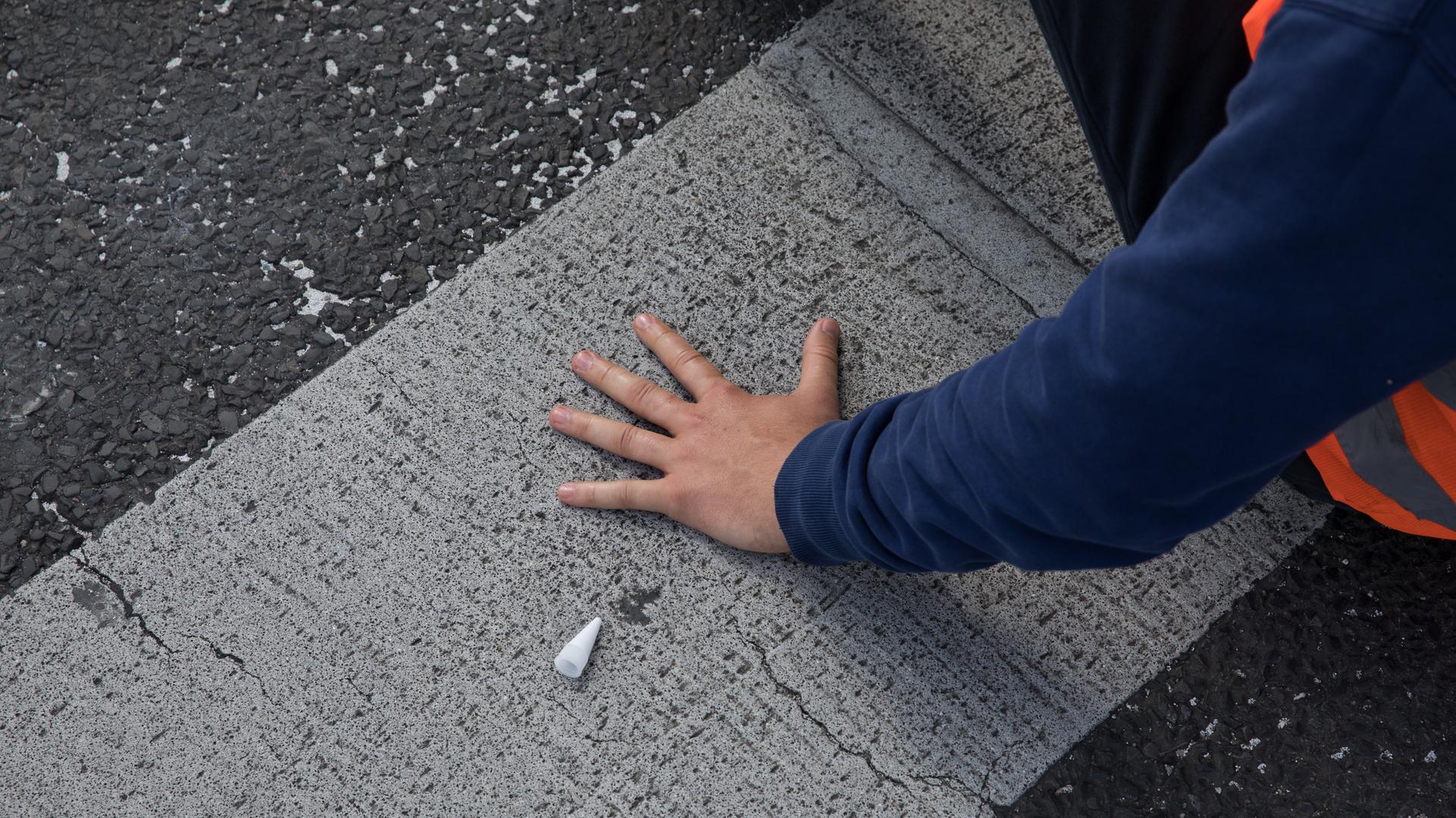 Ein Aktivist der Gruppe "Letzte Generation" hat seine linke Hand auf eine Straße geklebt, um diese zu blockieren.