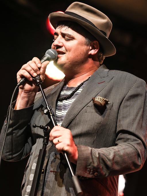 Ein Mann im grauen Anzug und Hut steht auf einer Bühne und singt mit geschlossenen Augen. Es ist der Brite Peter Doherty.
