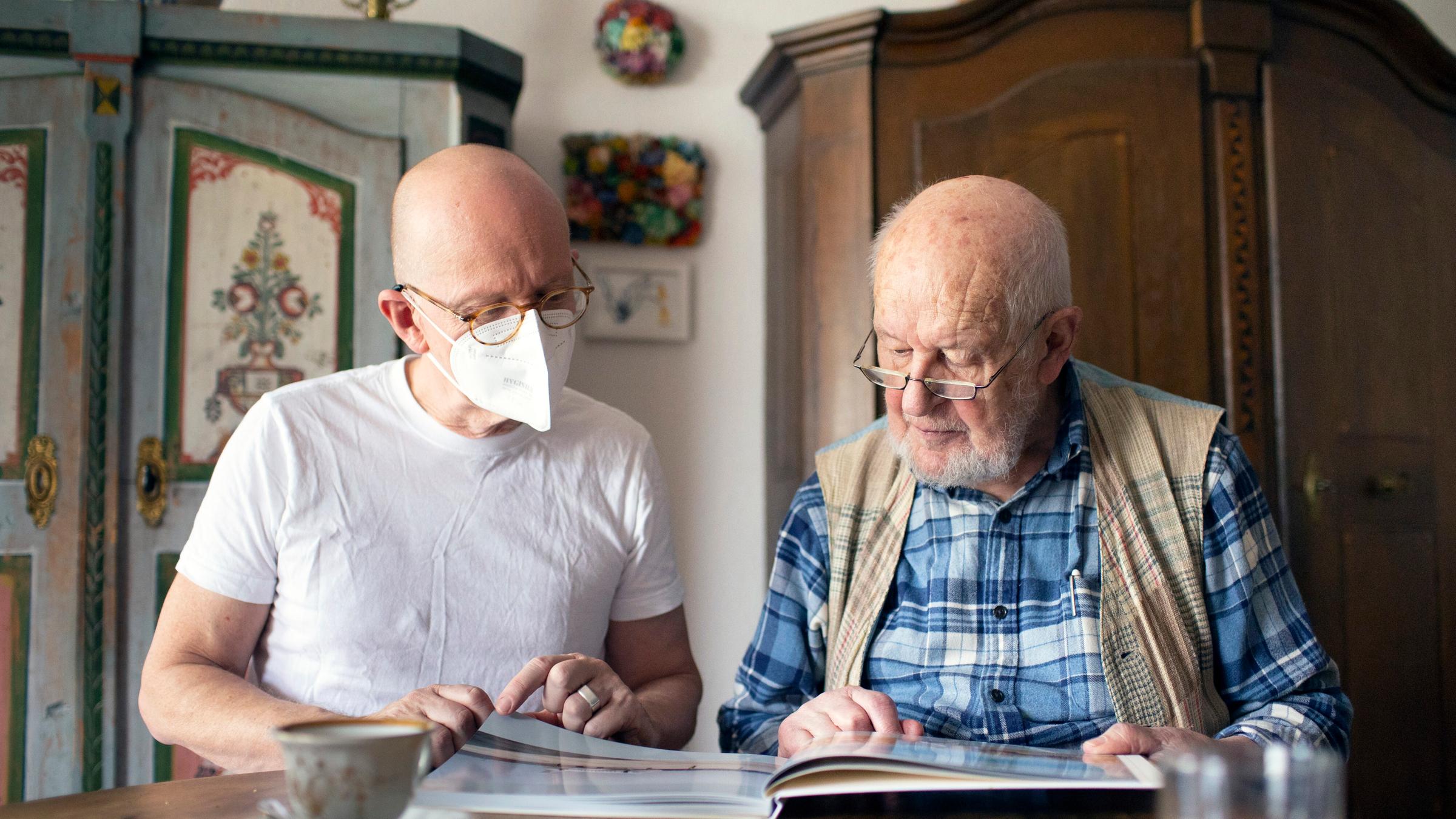 Ein Mann schaut mit einem Pflegebedürftigem in dessen Haus ein Fotobuch an 