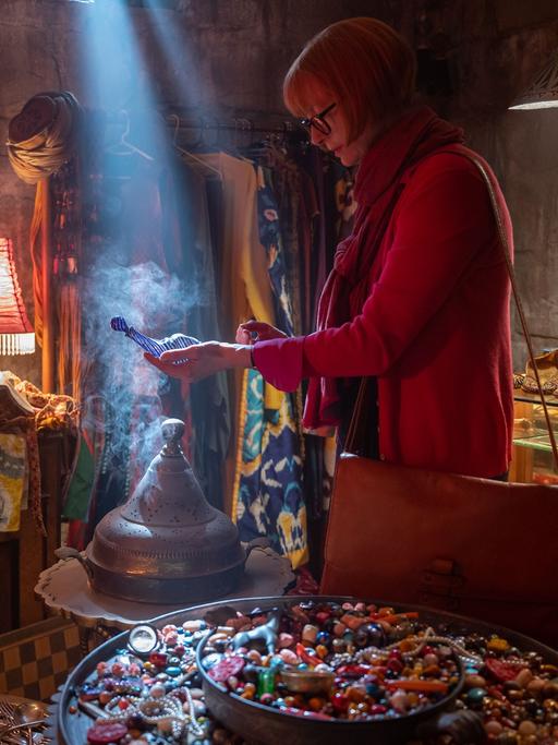 Szene aus dem Film "Three Thousand Years of Longing": Die Schauspielerin Tilda Swinton spielt Alithea, die in einer bunten, märchenhaften Umgebung einen flaschenähnlichen Gegenstand in der Hand hält. Aus diesem wird sie einen Dschinn befreien. 