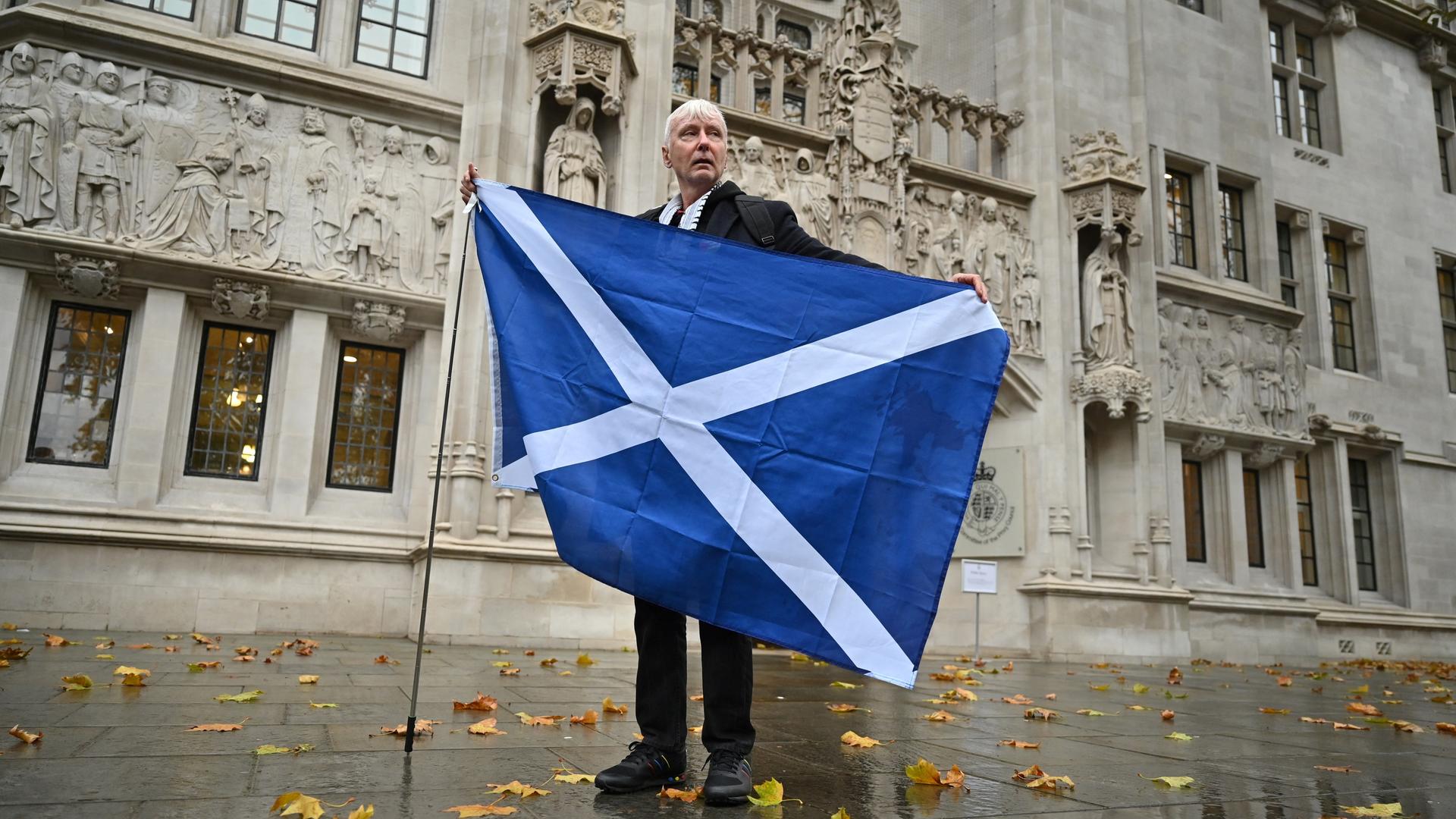 Ein Befürworter der schottischen Unabhängigkeit steht mit einer schottischen Flagge vor dem Gebäude des obersten britischen Gerichts in London. Ein Befürworter der schottischen Unabhängigkeit steht mit einer schottischen Flagge vor dem Gebäude des obersten britischen Gerichts in London.