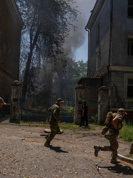 Ukrainische Soldaten bringen sich vor einem Angriff in Sicherheit. Man sieht den Rauch einer Rakete.