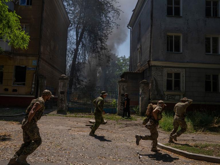 Ukrainische Soldaten bringen sich vor einem Angriff in Sicherheit. Man sieht den Rauch einer Rakete.
