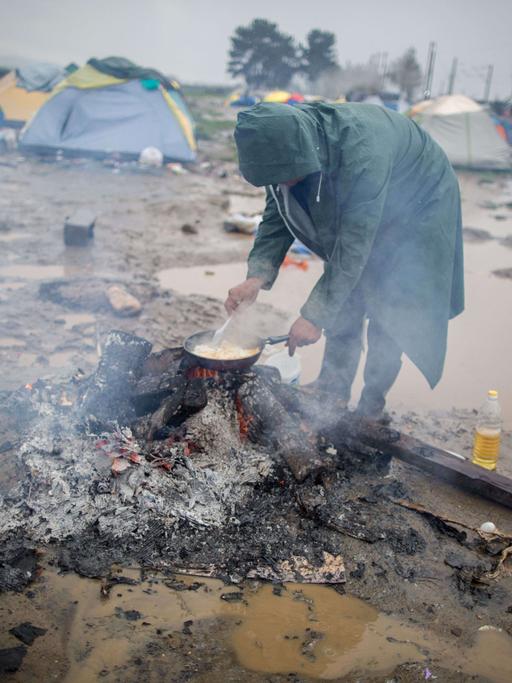 Ein Flüchtling brät am 13.03.2016 in Idomeni im Flüchtlingslager an der Grenze zwischen Griechenland und Mazedonien im strömenden Regen Eier. Nachdem die Balkanroute geschlossen wurde, lebten in diesem Lager zeitweise rund 12.500 Geflüchtete. 