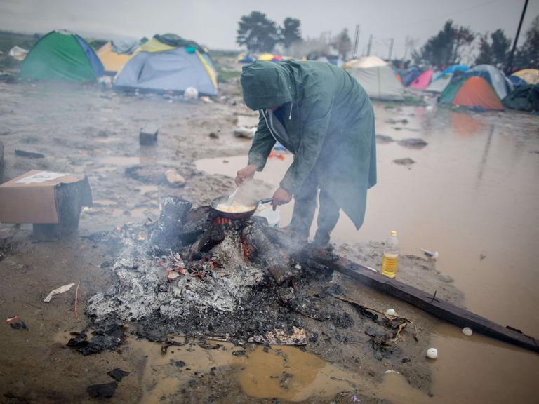 Ein Flüchtling brät am 13.03.2016 in Idomeni im Flüchtlingslager an der Grenze zwischen Griechenland und Mazedonien im strömenden Regen Eier. Nachdem die Balkanroute geschlossen wurde, lebten in diesem Lager zeitweise rund 12.500 Geflüchtete. 
