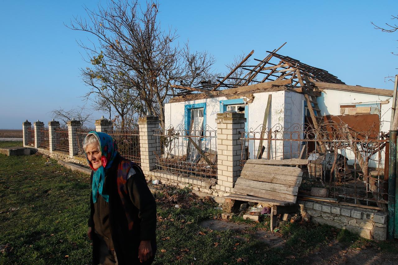 Eine ältere ukrainische Frau vor ihrem Haus in einem Dorf, das durch militärische Auseinandersetzungen stark beschädigt wurde.