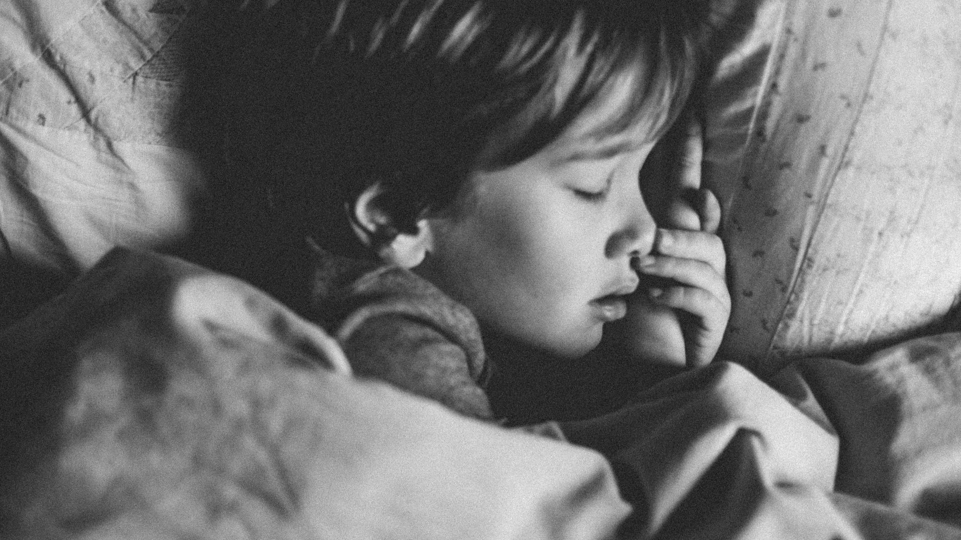 Ein Kind liegt mit geschlossenen Augen im Bett. Ein Kind liegt mit geschlossenen Augen im Bett.