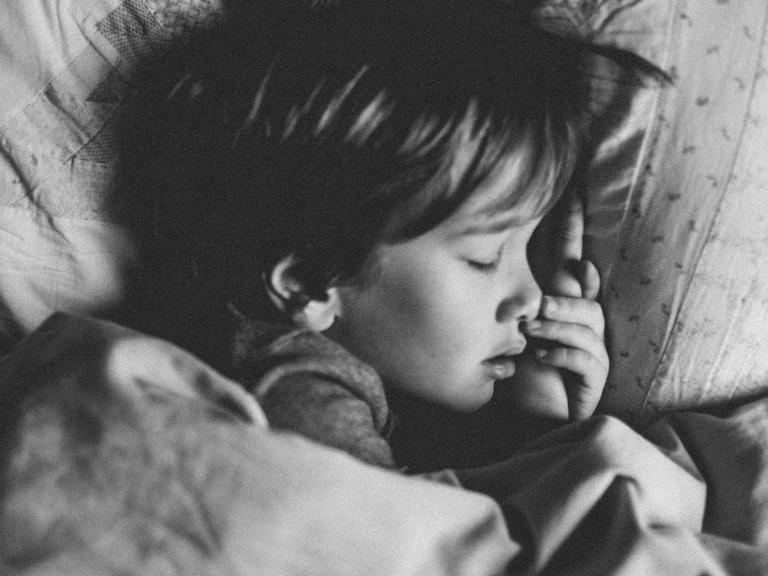 Ein Kind liegt mit geschlossenen Augen im Bett.