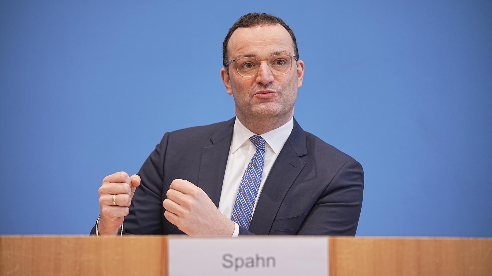 Spahn sitzt vor der blauen Wand auf dem Podium der Bundespressekonferenz und spricht zu Medienvertreter*innen. Spahn sitzt vor der blauen Wand auf dem Podium der Bundespressekonferenz und spricht zu Medienvertreter*innen.