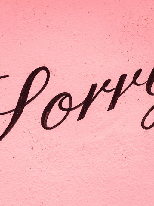 Auf einer rosafarbenen Wand steht in schwarzer Schrift "Sorry".