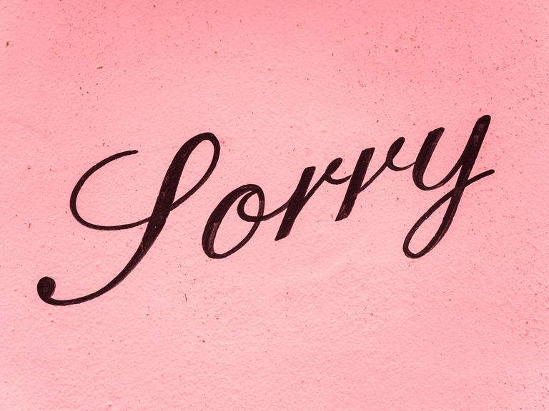 Auf einer rosafarbenen Wand steht in schwarzer Schrift "Sorry".