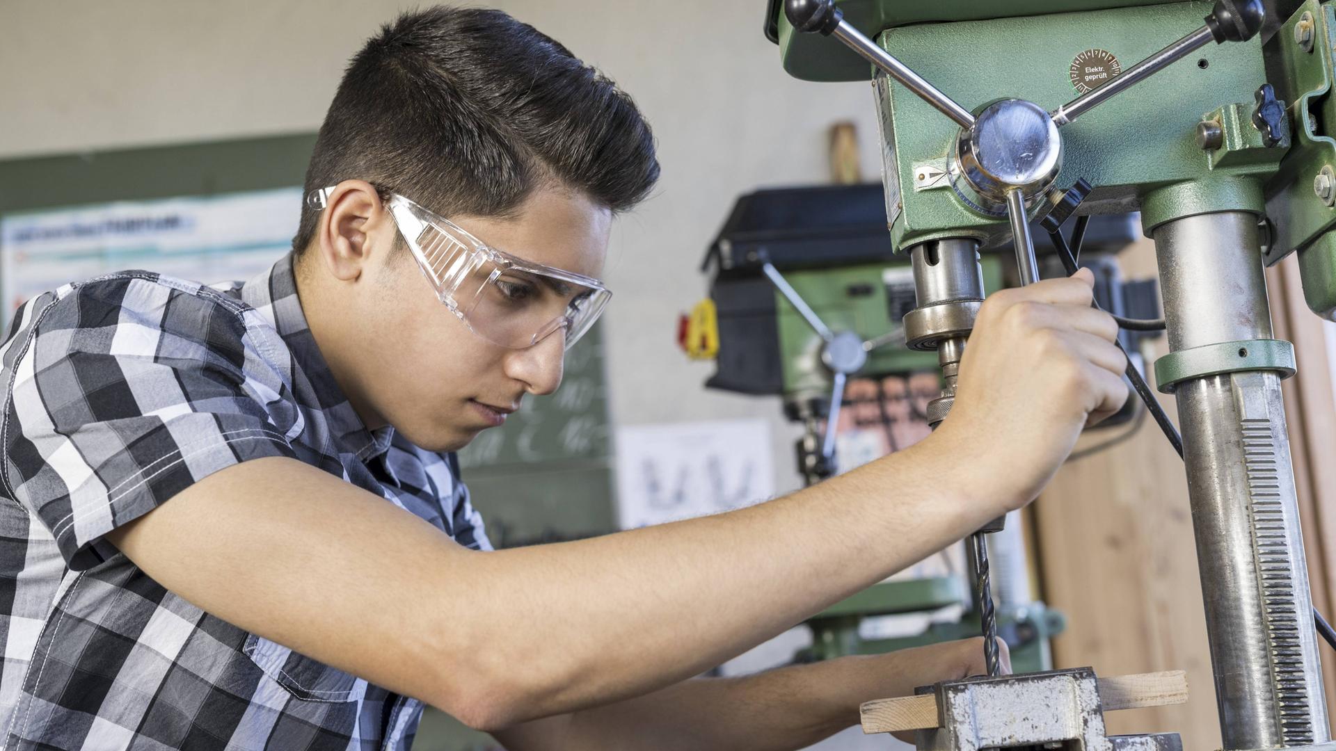 Ein Auszubildender mit Schutzbrille arbeitet in einem Werkraum. Ein Auszubildender mit Schutzbrille arbeitet in einem Werkraum.