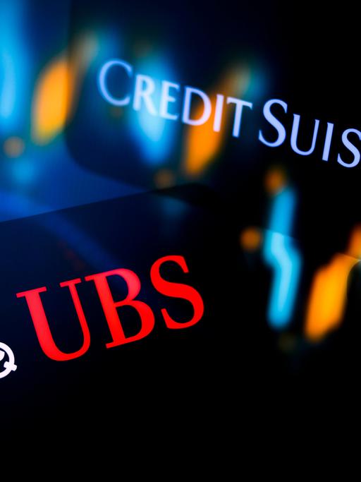 Leuchtende Logos der Banken UBS und Credit Suisse auf dunklem Hintergrund