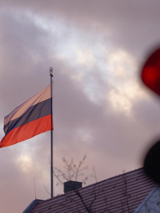 Die Flagge der Russischen Botschaft weht am frühen Morgen vor einer roten Ampel. Die russische Armee ist am frühen Morgen in die Ukraine einmarschiert.