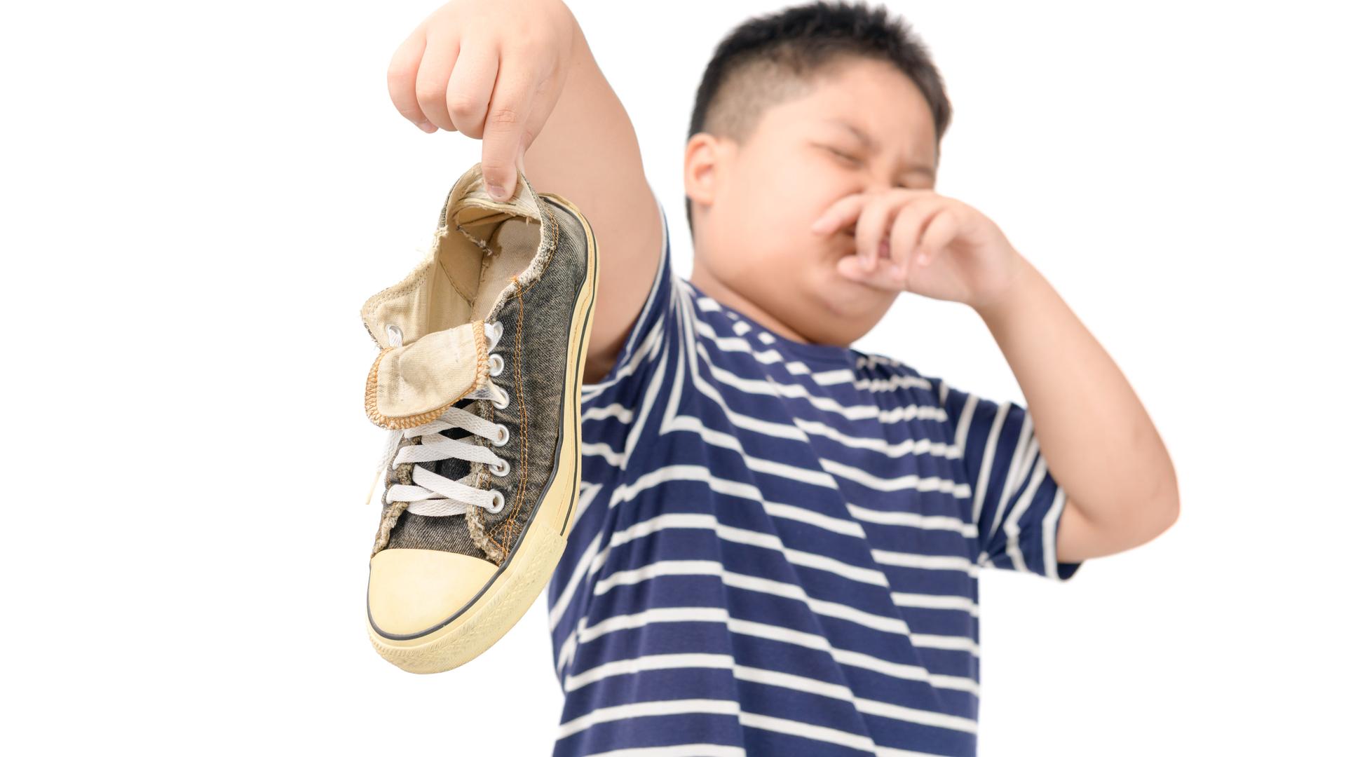 Ein Kind hält einen Turnschuh mit ausgestrecktem Arm nach vorne. Mit der anderen Hand hält es sich die Nase zu. Die Augen sind geschlossen. Ein Kind hält einen Turnschuh mit ausgestrecktem Arm nach vorne. Mit der anderen Hand hält es sich die Nase zu. Die Augen sind geschlossen.