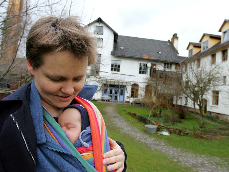 Ina, Bewohnerin der Kommune im nordhessischen Kaufungen, hält ihren  Sohn Milan in einem Tragetuch. In der Kommune Niederkaufungen gibt es eine Tagespflegeeinrichtung. Die Altenstation steht sowohl den in die Jahre gekommenen Mitgliedern der Kommune und ihren Angehörigen sowie Menschen von außerhalb offen. Deren Grundprinzipien sind ein gemeinsames Wirtschaften mit dem Verzicht auf Privateigentum und im Konsens gefasste Entscheidungen. 