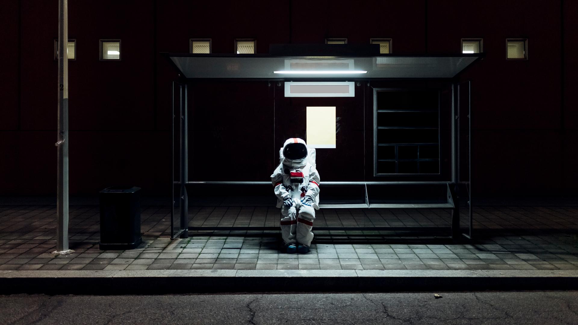 Ein Astronaut sitzt allein im Dunkeln an einer Bushaltestelle.