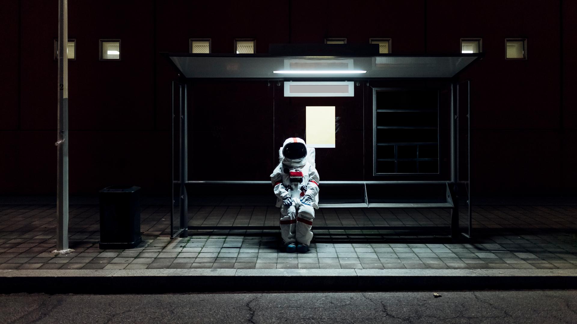 Ein Astronaut sitzt allein im Dunkeln an einer Bushaltestelle. Ein Astronaut sitzt allein im Dunkeln an einer Bushaltestelle.