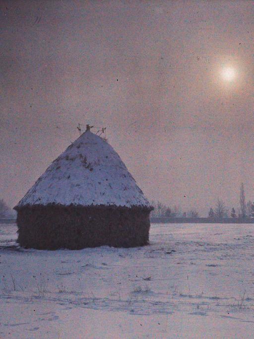 Auf einer frühen Fotografie steht eine Hütte im Schnee vor fahler Sonne.