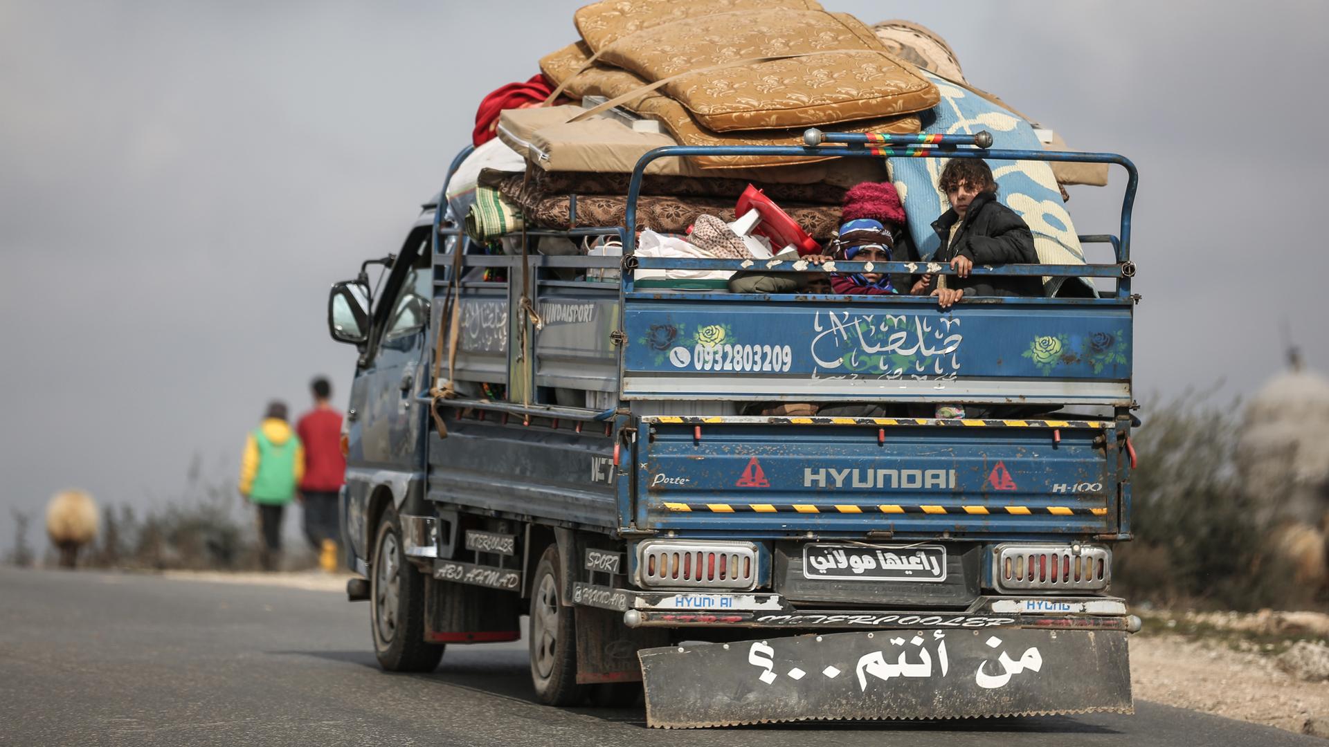 Eine syrische Familie sitzt mit ihren Habseligkeiten auf der Ladefläche eines Lastwagens während der Flucht aus Idlib, 2020.