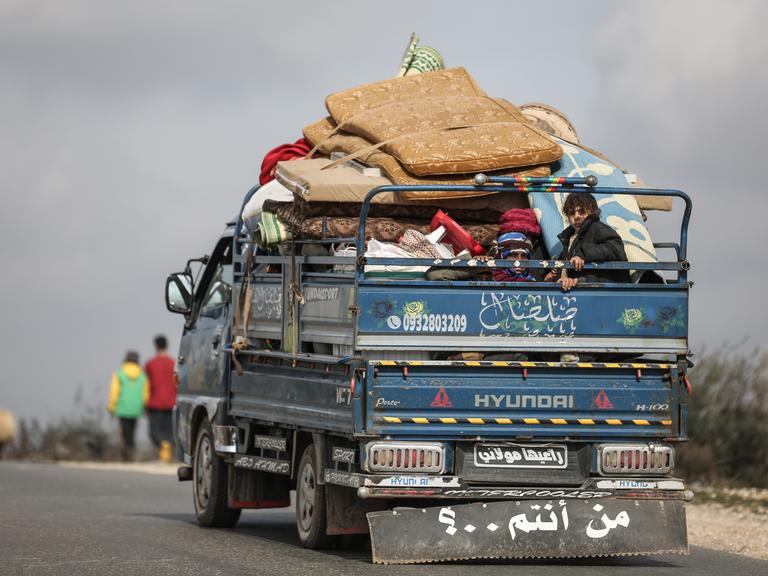Eine syrische Familie sitzt mit ihren Habseligkeiten auf der Ladefläche eines Lastwagens während der Flucht aus Idlib, 2020.
