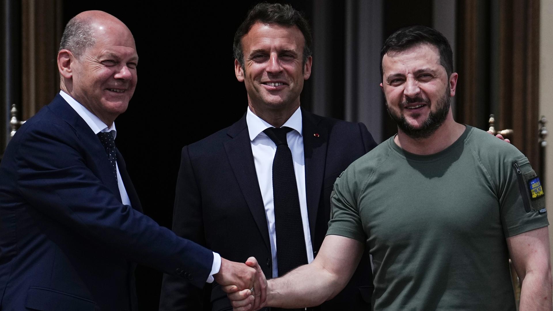 Bundes-Kanzler Olaf Scholz schüttelt die Hand vom dem Präsidenten von der Ukraine. Er heißt Wolodymyr Selenskyj. In der Mitte steht der Präsident von dem Land Frankreich. Er heißt Emmanuel Macron. Bundes-Kanzler Olaf Scholz schüttelt die Hand vom dem Präsidenten von der Ukraine. Er heißt Wolodymyr Selenskyj. In der Mitte steht der Präsident von dem Land Frankreich. Er heißt Emmanuel Macron.