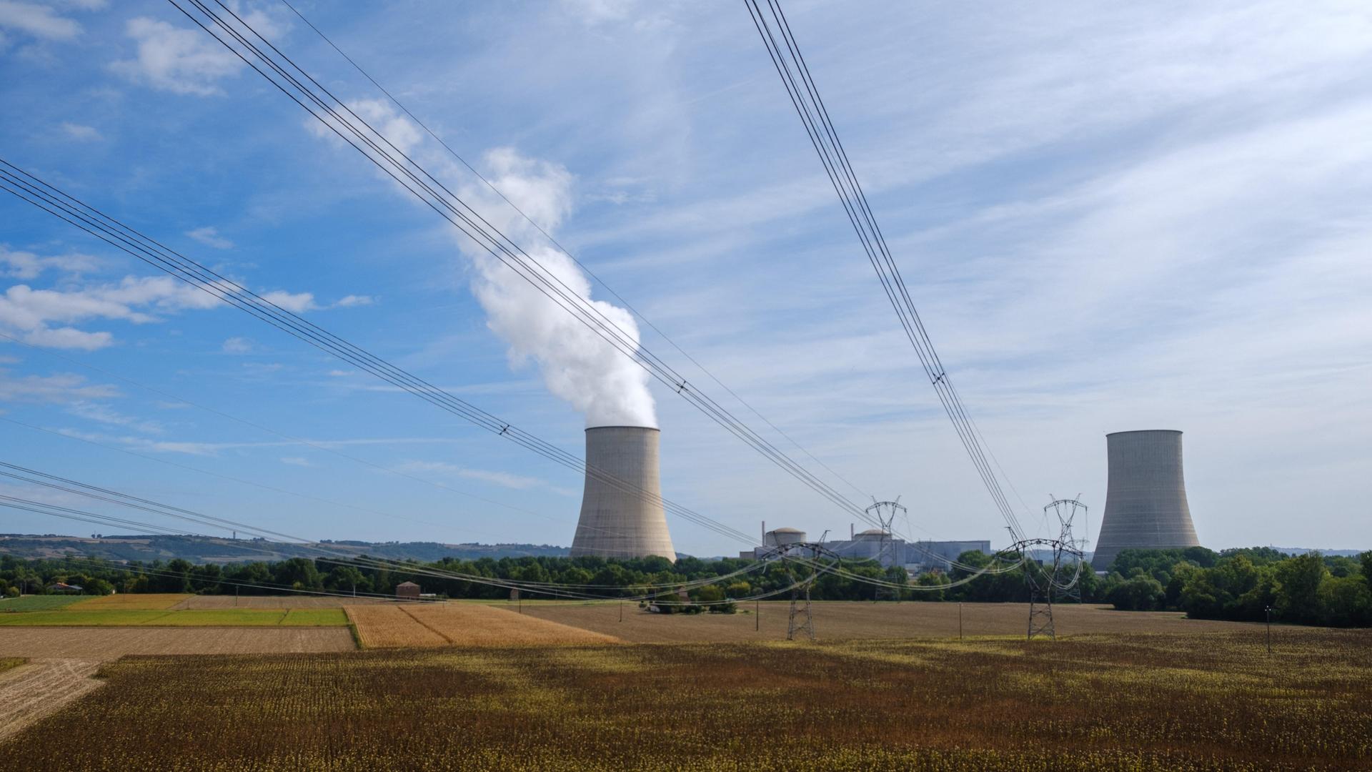 Blick über ein Getreidefeld auf zwei Kühltürme eines Atomkraftwerks in Frankreich, aus einem davon steigt Dampf auf, Hochspannungsleitugen durchschneiden den Himmel. Blick über ein Getreidefeld auf zwei Kühltürme eines Atomkraftwerks in Frankreich, aus einem davon steigt Dampf auf, Hochspannungsleitugen durchschneiden den Himmel.