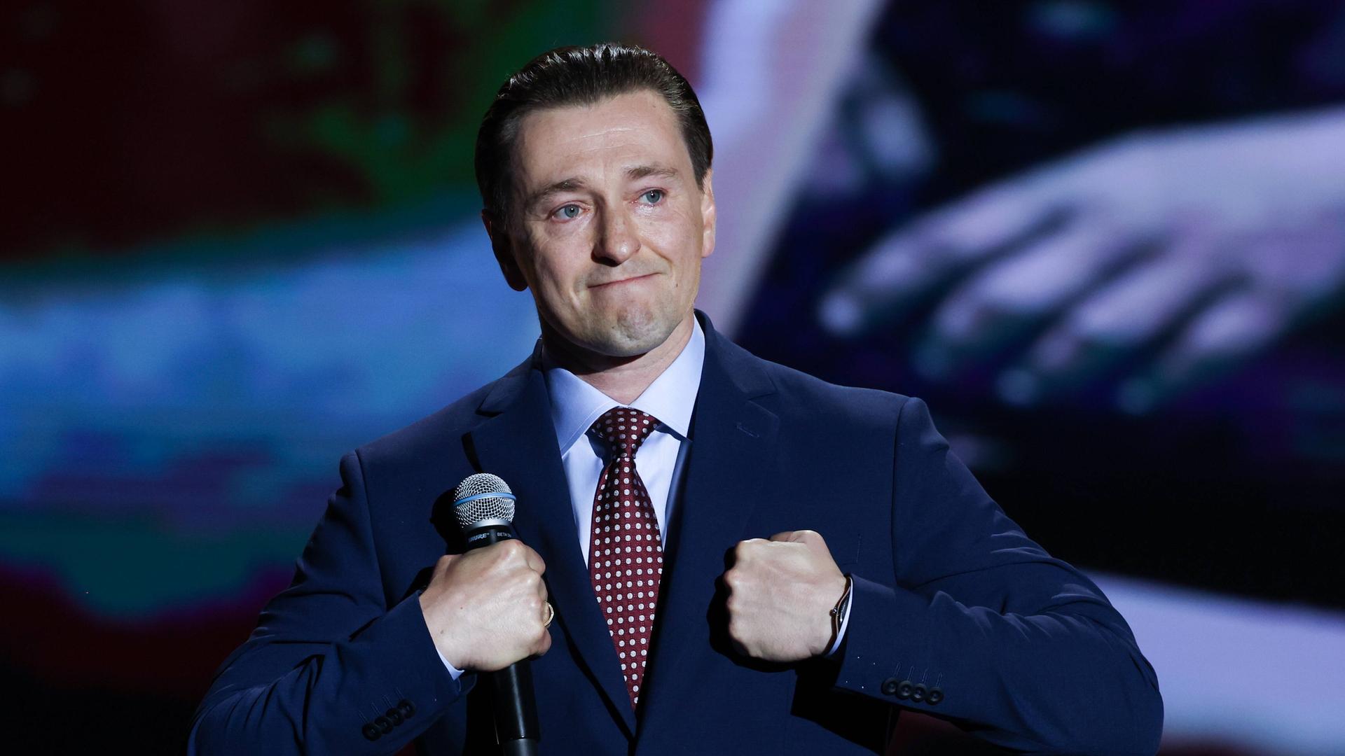 Sergei Besrukow steht mit dem Mikrofon in der Hand auf einer Bühne und macht einen bewegten Gesichtsausdruck.