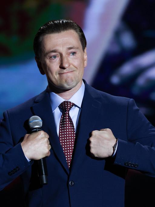 Sergei Besrukow steht mit dem Mikrofon in der Hand auf einer Bühne und macht einen bewegten Gesichtsausdruck.