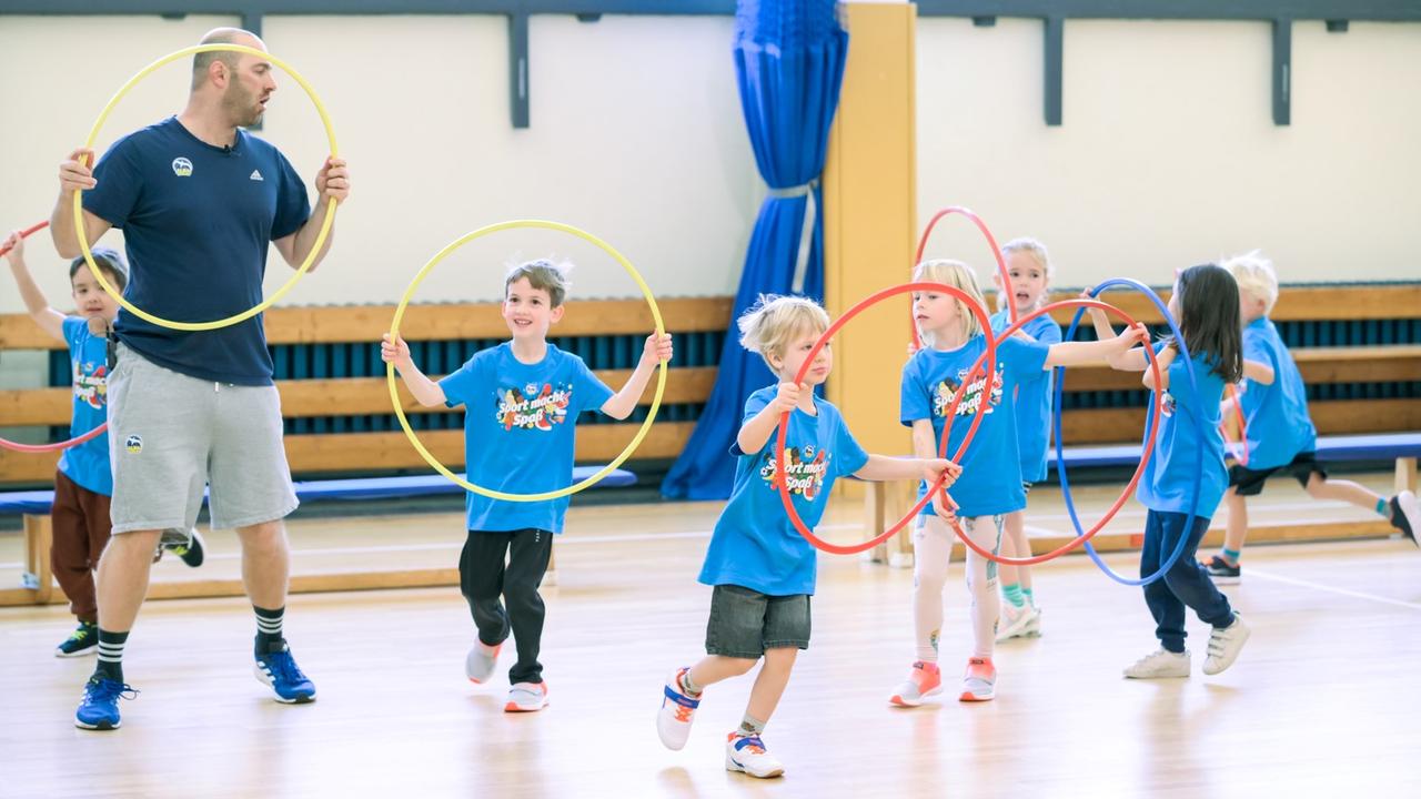 Ein Trainer zeigt den Kindern Übungen mit dem Hula-Hoop-Reifen. Ein Trainer zeigt den Kindern Übungen mit dem Hula-Hoop-Reifen.