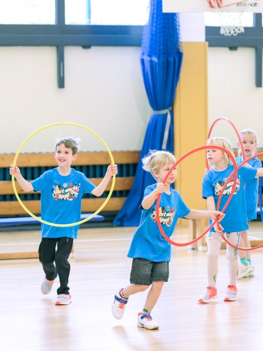 Ein Trainer zeigt den Kindern Übungen mit dem Hula-Hoop-Reifen.